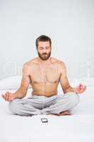 Man doing yoga while listening to music on bed