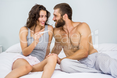 Happy couple looking at pregnancy test on bed