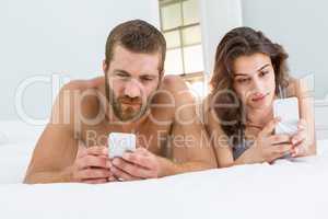 Man and woman using mobile phone on bed