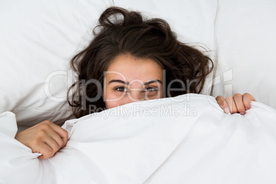 Woman hiding under blanket on bed