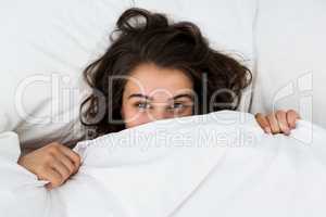 Woman hiding under blanket on bed