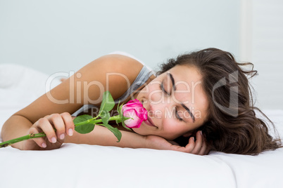 Woman smelling a rose flower on bed