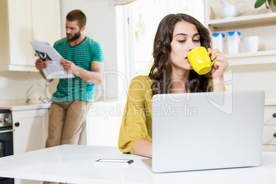 Woman having coffee while using laptop