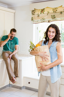 Woman holding groceries while man talking on mobile phone in kit