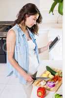 Young woman using digital tablet while chopping vegetables