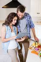 Woman using digital tablet and man chopping vegetables