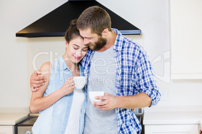 Young couple holding cup of coffee in kitchen