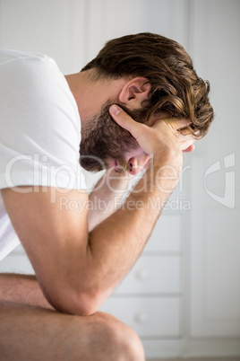 Worried man with hand on forehead sitting on bed