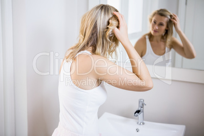 Young woman checking her hair in bathroom mirror