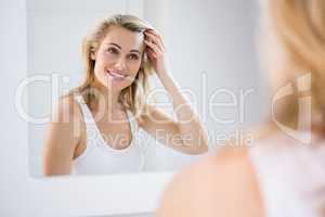 Young woman checking her hair in bathroom mirror