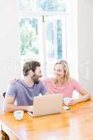 Couple looking at each other while using laptop