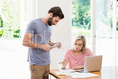 Man cutting a credit card while tense woman with bills sitting a