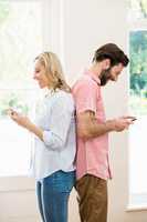Couple standing back to back and text messing on mobile phone