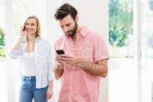 Man texting messaging while woman talking on mobile phone