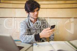 Young student sitting at desk and using mobile phone