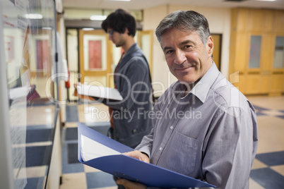 Portrait of smiling professor standing in front of notice board