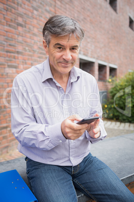 Portrait of smiling professor using mobile phone in campus