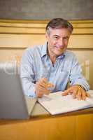 Portrait of happy professor writing in book at desk