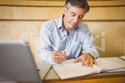 Professor writing in book at desk