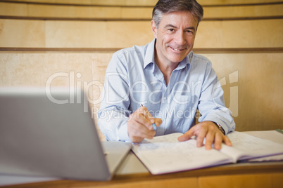Portrait of happy professor writing in book at desk