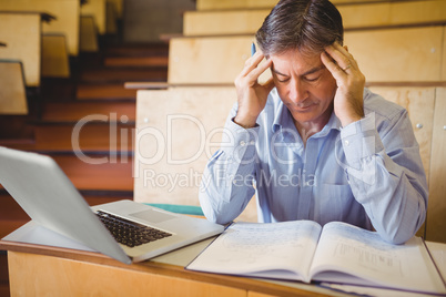 Depressed professor sitting with notes and laptop