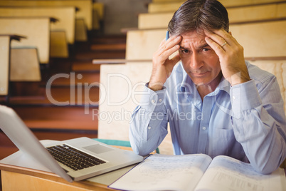 Depressed professor sitting with notes and laptop