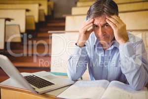 Depressed professor sitting with notes and laptop