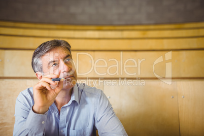 Thoughtful professor sitting at desk with pen