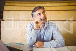 Thoughtful professor sitting at desk with book and laptop