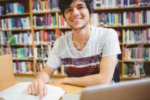 Happy young student sitting at desk reading a book