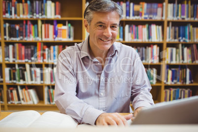 Portrait of happy professor sitting at desk using laptop