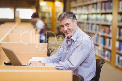 Portrait of happy professor sitting at desk using his laptop