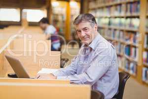 Portrait of happy professor sitting at desk using his laptop