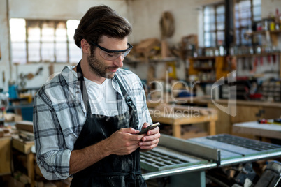 Carpenter texting someone and wearing protective glasses