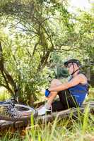 Senior man is sitting down beside his bike in a forest