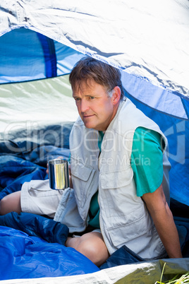 senior man holding a cup of coffee and is sitting in his tent