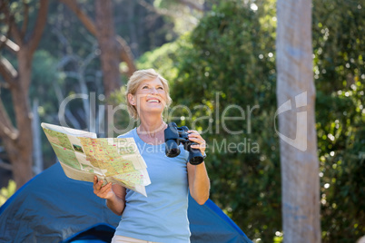 Mature woman smiling and holding binoculars and map