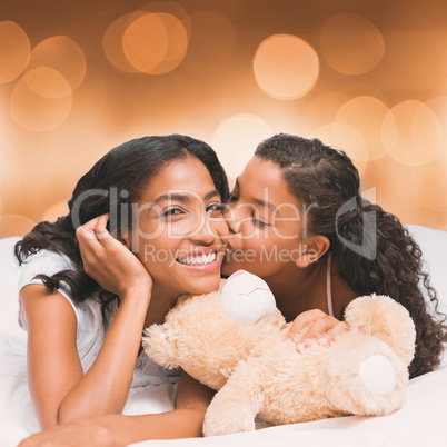 Composite image of pretty woman lying on bed with her daughter kissing cheek