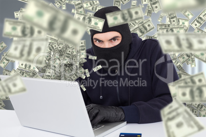 Composite image of hacker in balaclava hacking a laptop