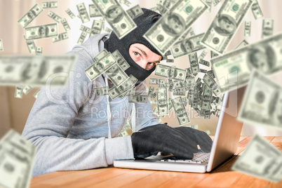 Composite image of focused thief with hood typing on laptop