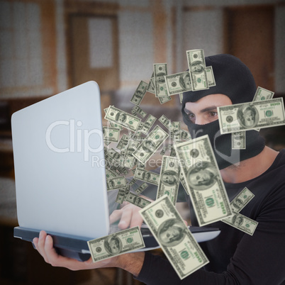 Composite image of focused burglar with balaclava holding laptop