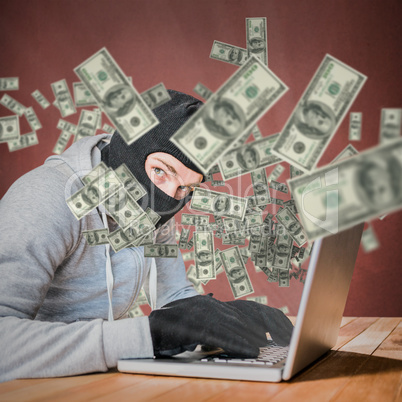 Composite image of focused thief with hood typing on laptop