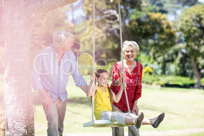 Grandparents pushing their granddaughter on swing