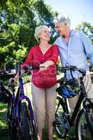 Senior couple standing with bicycle in park