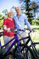 Senior couple standing with bicycle in park