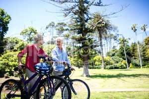 Senior couple walking with bicycle in park