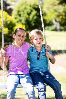 Siblings sitting on a swing in the park