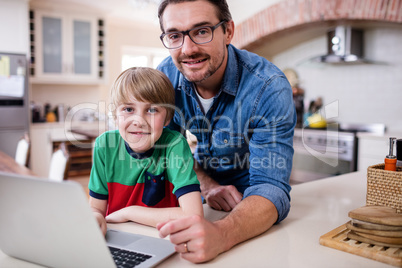 Portrait of father and son using laptop in kitchen