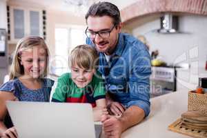 Father and kids using laptop in kitchen
