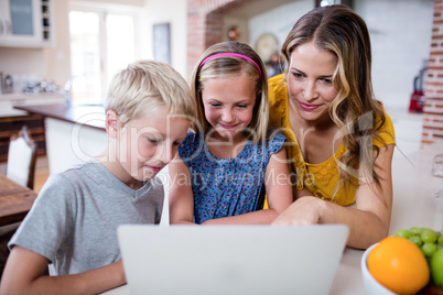 Mother and kids using laptop in kitchen